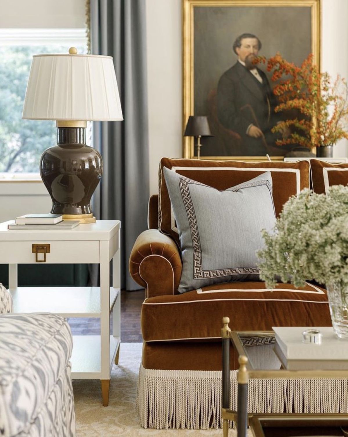 Refined living space with velvet fringe-trimmed sofa, neoclassical accents, and a stately portrait in a gilded frame — styled by JohnRoss.